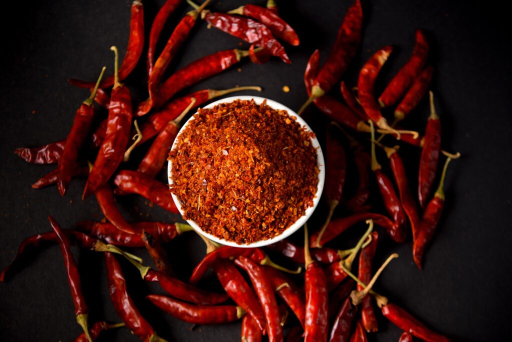 Red chili powder and whole chilies on dark background, showcasing spice and flavor.